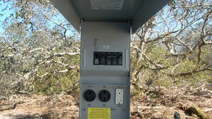 An electrical box with a warning sign, surrounded by dry branches and trees. - SPACIOUS COVERED RV LOT WITH A LARGE CONCRETE PAD (Port Saint Joe)