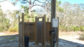 A wooden structure with a door, a trash bin, and a utility box. - SPACIOUS COVERED RV LOT WITH A LARGE CONCRETE PAD (Port Saint Joe)