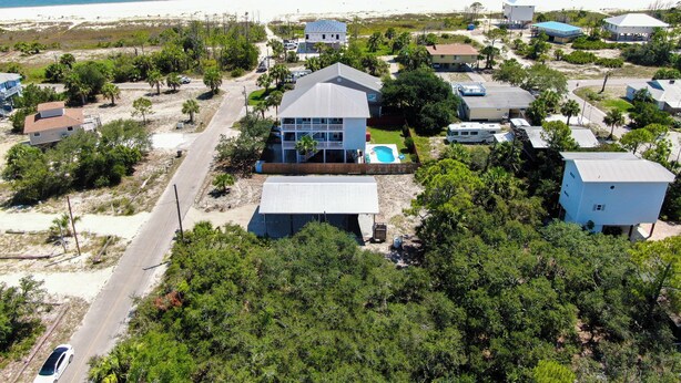 A coastal residential area with a prominent house featuring a swimming pool, surrounded by other houses and vegetation. - SPACIOUS COVERED RV LOT WITH A LARGE CONCRETE PAD (Port Saint Joe)