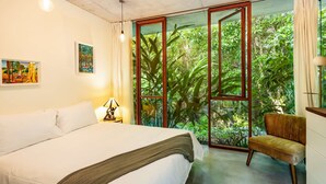 A bedroom with a bed, a chair, a nightstand, and a window with a view of greenery. - The Planchonella House - Eco Stay de Luxe (Edge Hill)