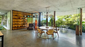 A spacious room with a round dining table and chairs, a bookshelf, and a view of greenery outside. - The Planchonella House - Eco Stay de Luxe (Edge Hill)