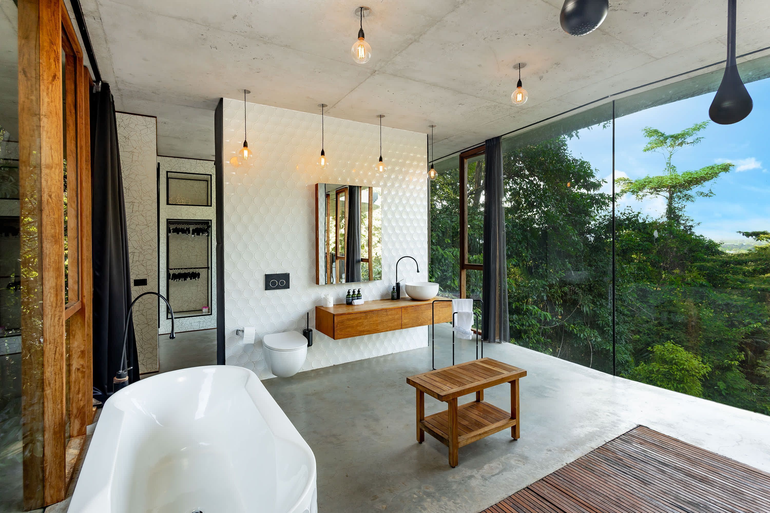 Un baño moderno con una bañera independiente, un tocador de madera, un espejo grande y vistas al exterior.