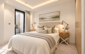 A bedroom with a bed, bedside tables, a painting, and a view through a glass door.