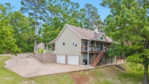 A two-story house with a covered front porch, a stone retaining wall, and a driveway leading to a garage. - Lakeside Hideaway, Fire-Pit | Near Marina (Rogers)