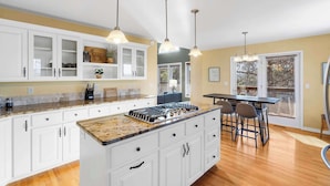 A modern kitchen with white cabinetry, granite countertops, and pendant lighting. - Lakeside Hideaway, Fire-Pit | Near Marina (Rogers)