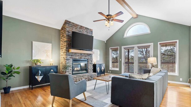 A living room with a stone fireplace, a ceiling fan, and a large window. - Lakeside Hideaway, Fire-Pit | Near Marina (Rogers)