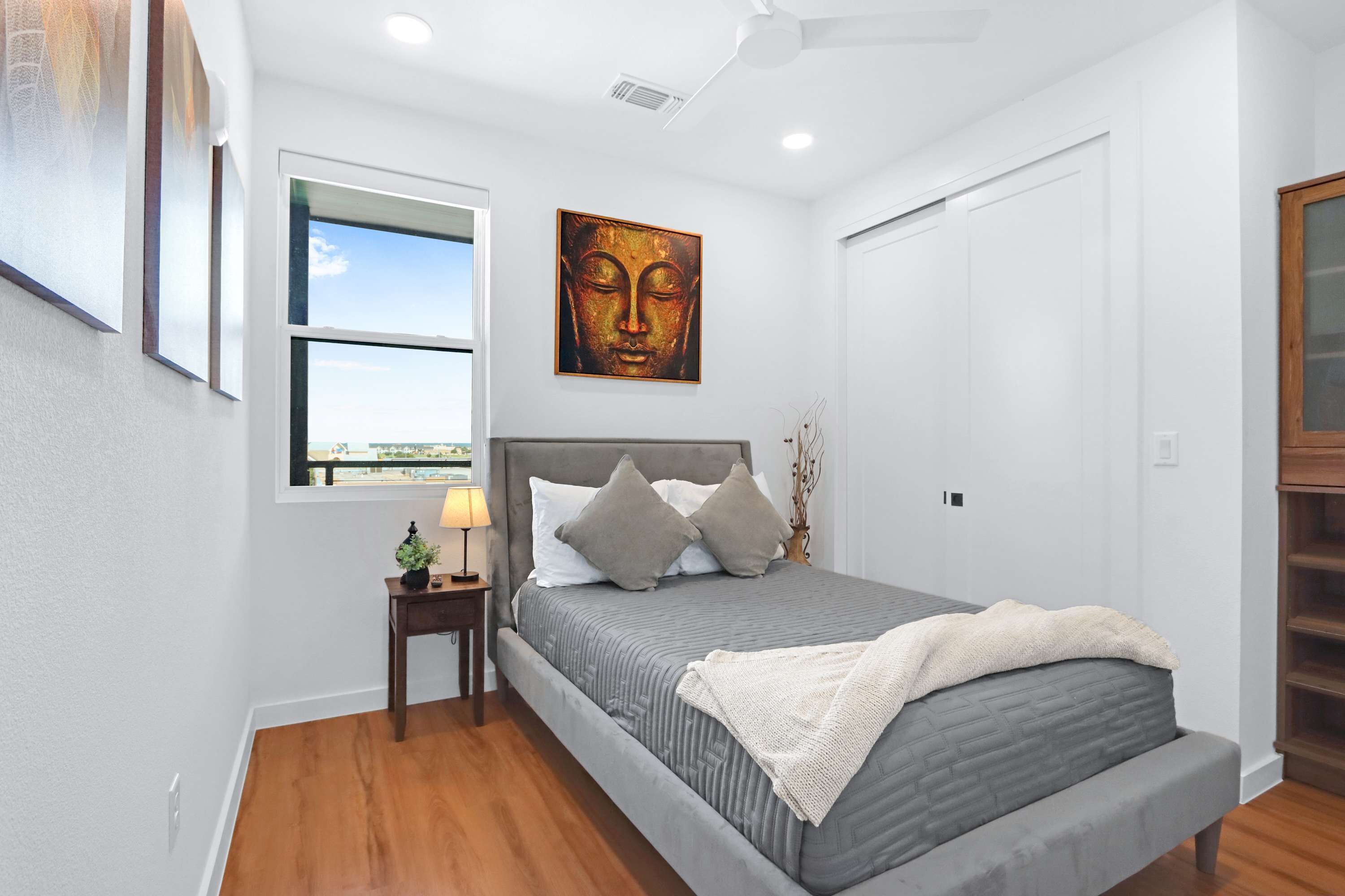 Un dormitorio con cama, mesita de noche, ventana, ventilador de techo y una obra de arte en la pared.