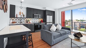 A modern kitchen with dark cabinets, a white countertop, and a dining area with a table and chairs. - Modern Hill Country Condo for 4 w/ Resort Perks! (New Braunfels)
