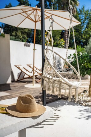 A hammock chair, a sun umbrella, and a straw hat on a table. - Villa Lafleur (Châteaurenard)