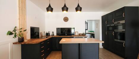 A modern kitchen with black cabinetry, a wooden countertop, and three pendant lights.