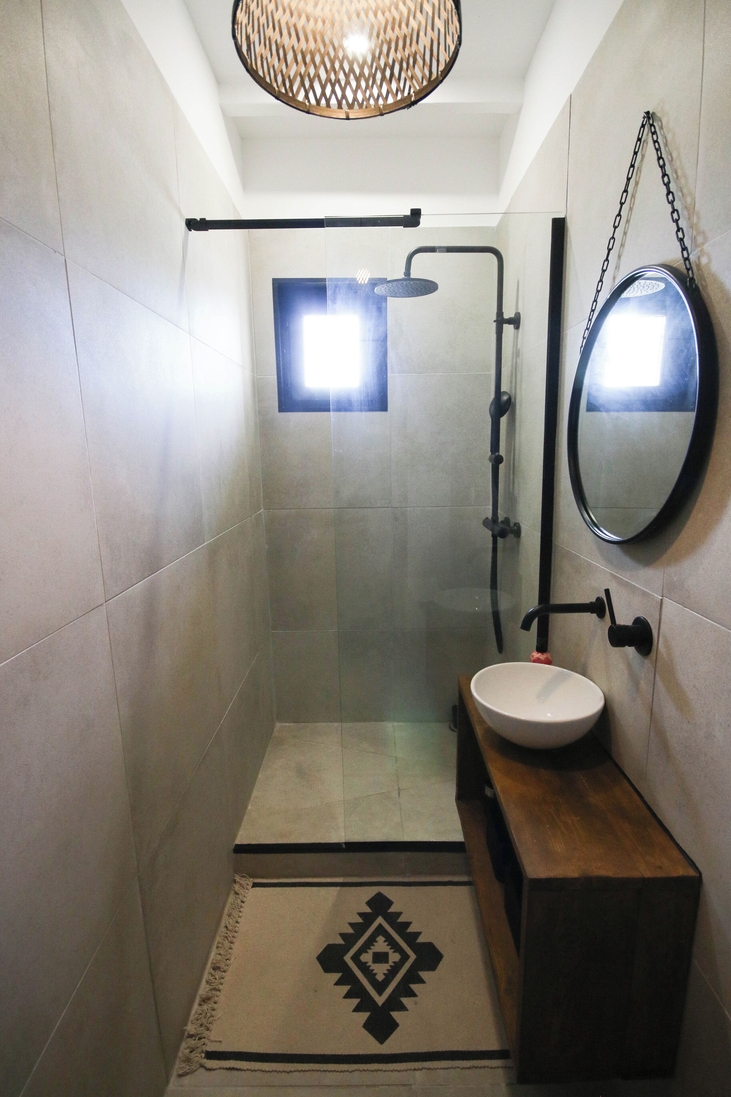 A small, modern bathroom with a shower, a round mirror, and a wooden vanity.