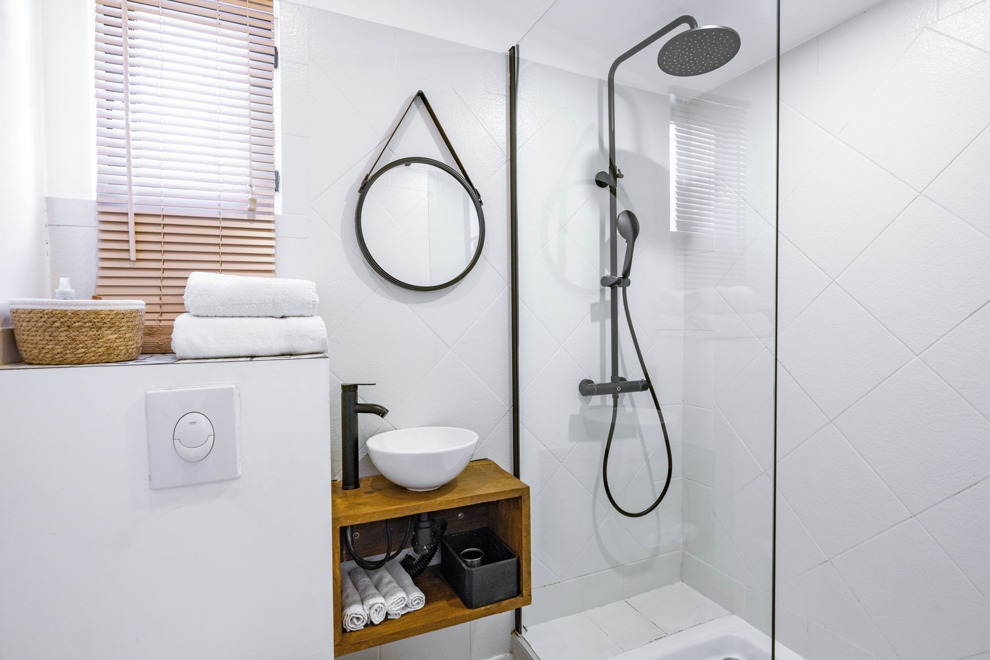 A modern bathroom with a glass-enclosed shower, a white sink, and a wooden shelf with towels.