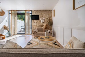 A modern living room with a stone wall, a sofa, a coffee table, and a TV mounted on the wall. - Villa Lafleur (Châteaurenard)
