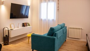Ein modernes Wohnzimmer mit einem blaugrünen Sofa, einem flachbildfernseher an der Wand, einem kleinen gelben Tisch und einer Heizung.