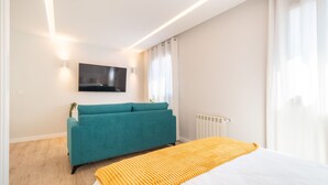 Ein modernes Schlafzimmer mit Bett, einem türkisfarbenen Sofa, einem an der Wand montierten Fernseher und einer Heizung.