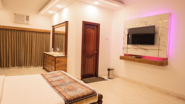 Une chambre d’hôtel avec un lit, une commode en bois, un miroir, un téléviseur fixé au mur et une porte.