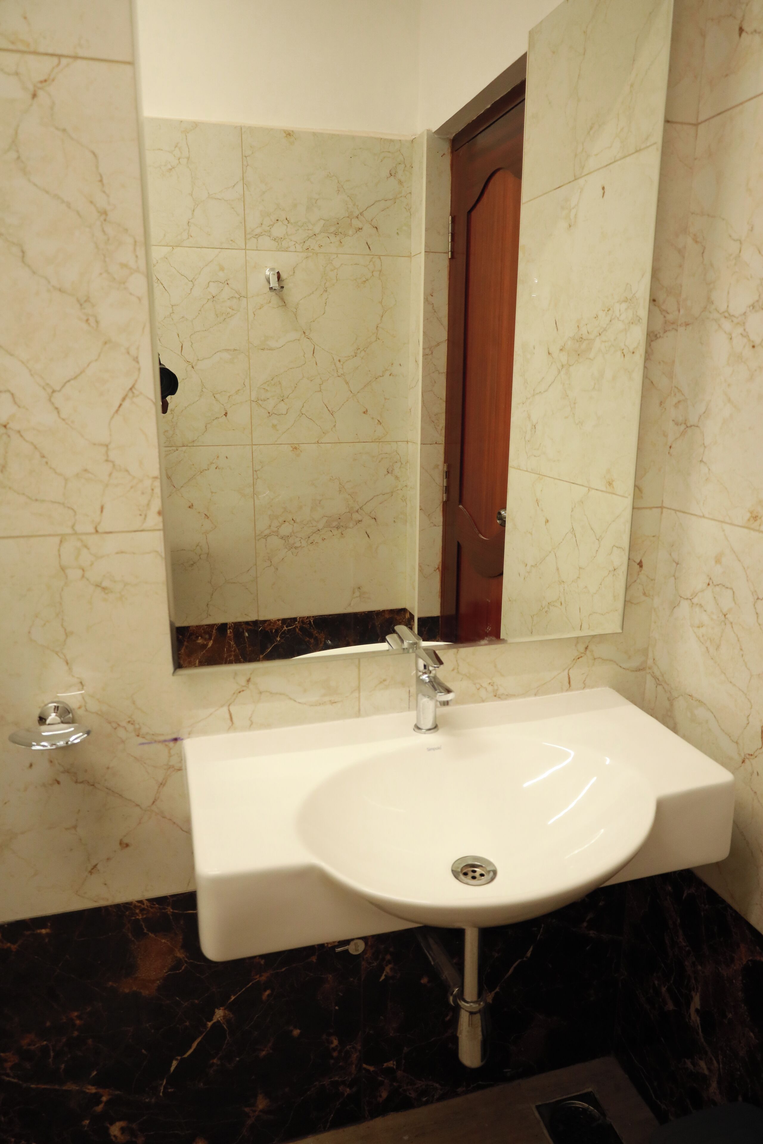 Une salle de bain avec un lavabo blanc, un miroir et un mur recouvert de carreaux de marbre.