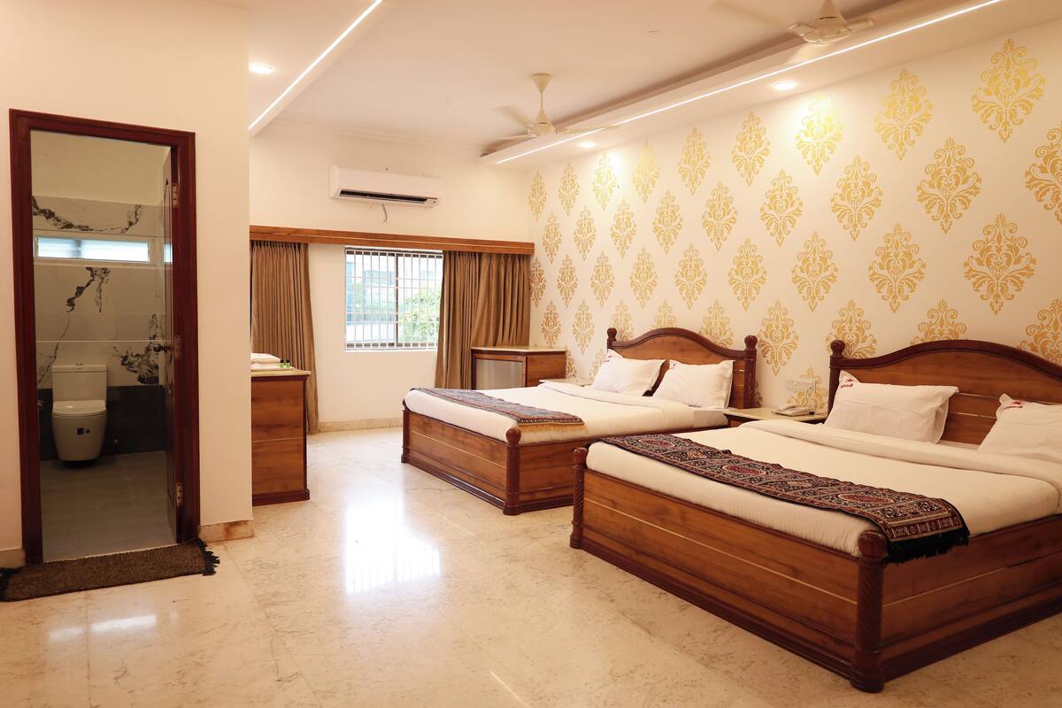 A hotel room with two wooden beds, a large mirror, a bathroom with a toilet and sink, and a patterned wall.