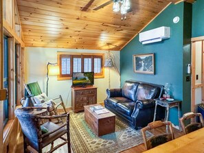 A cozy living room with a wooden ceiling, a leather sofa, a coffee table, and a television.