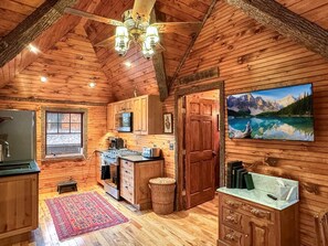 Ein gemütliches Blockhaus-Interieur mit einer Küche, einer Essecke und einem großen Fenster mit Blick auf eine gebirgige Landschaft.
