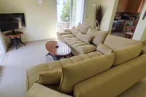 A living room with a sectional sofa, a coffee table, a television, and a kitchen area in the background. - Plaka Elounda ..private Pool ..2 Beds..jaccuzi..parking..spinalonga/sea Views (Agios Nikolaos)
