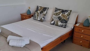 A neatly made bed with white linens, two decorative pillows with a leaf pattern, a folded towel on the bed, and a wooden nightstand with a blue vase on it. - Plaka Elounda ..private Pool ..2 Beds..jaccuzi..parking..spinalonga/sea Views (Agios Nikolaos)