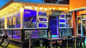Een restaurant met een neonreclame, terras en een motorfiets voor de deur.