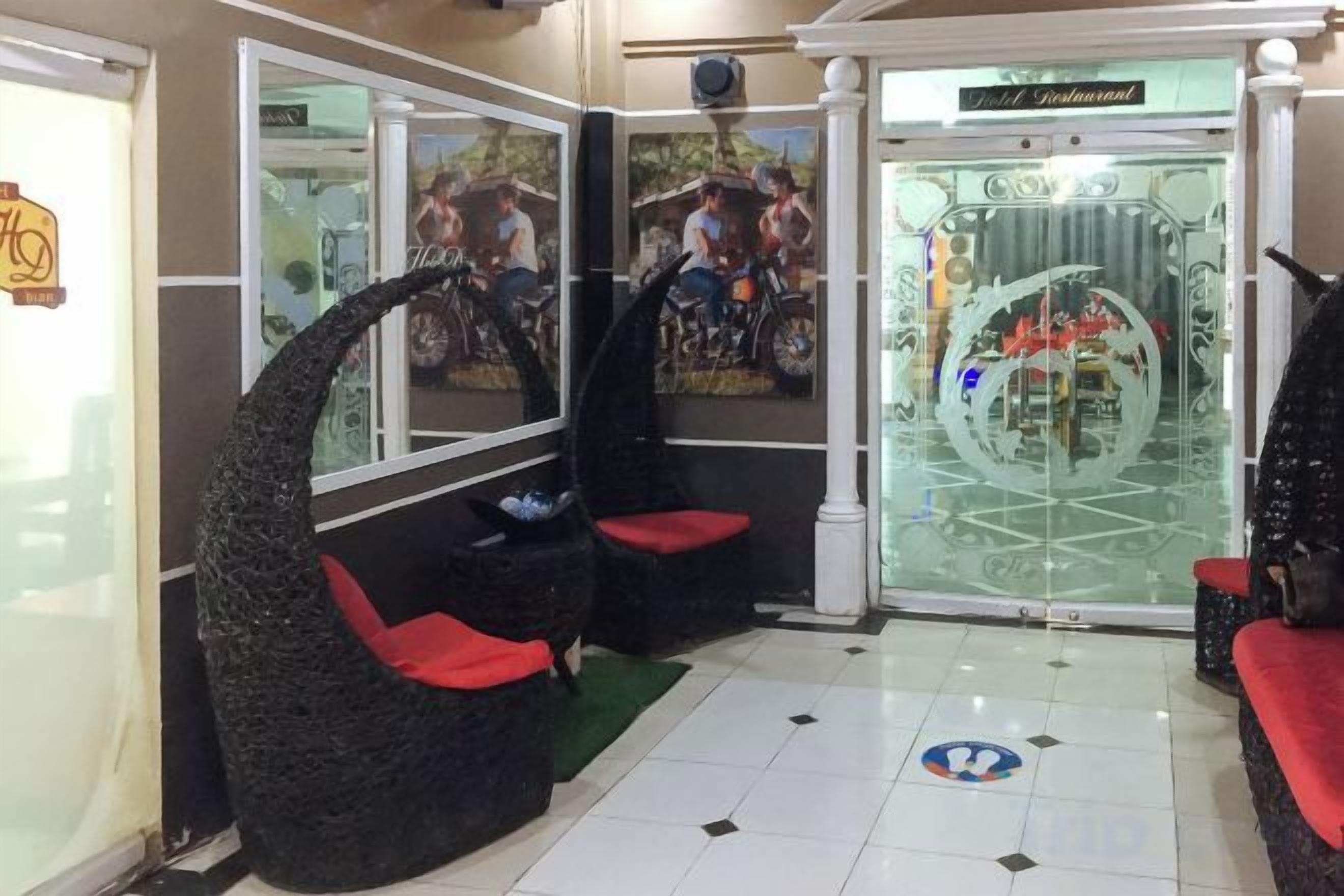 Um lobby com divisória de vidro, balcão de recepção e dois pufes pretos com almofadas vermelhas.