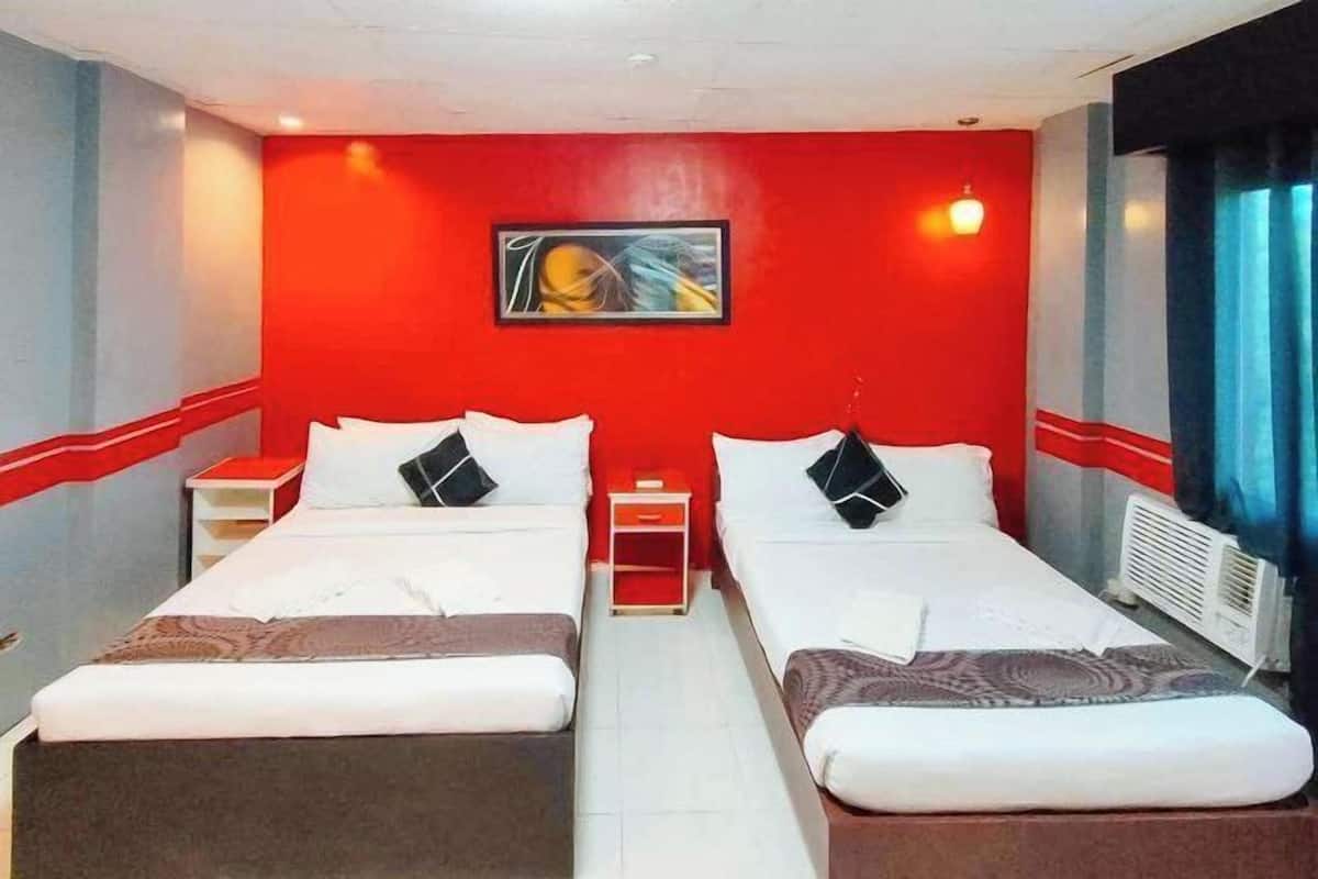 A hotel room with two beds, a red accent wall, a painting, and a window with curtains.