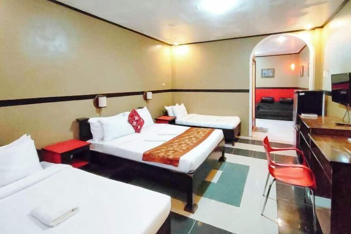 A hotel room with two single beds, a desk with a chair, a television, and a small kitchenette.