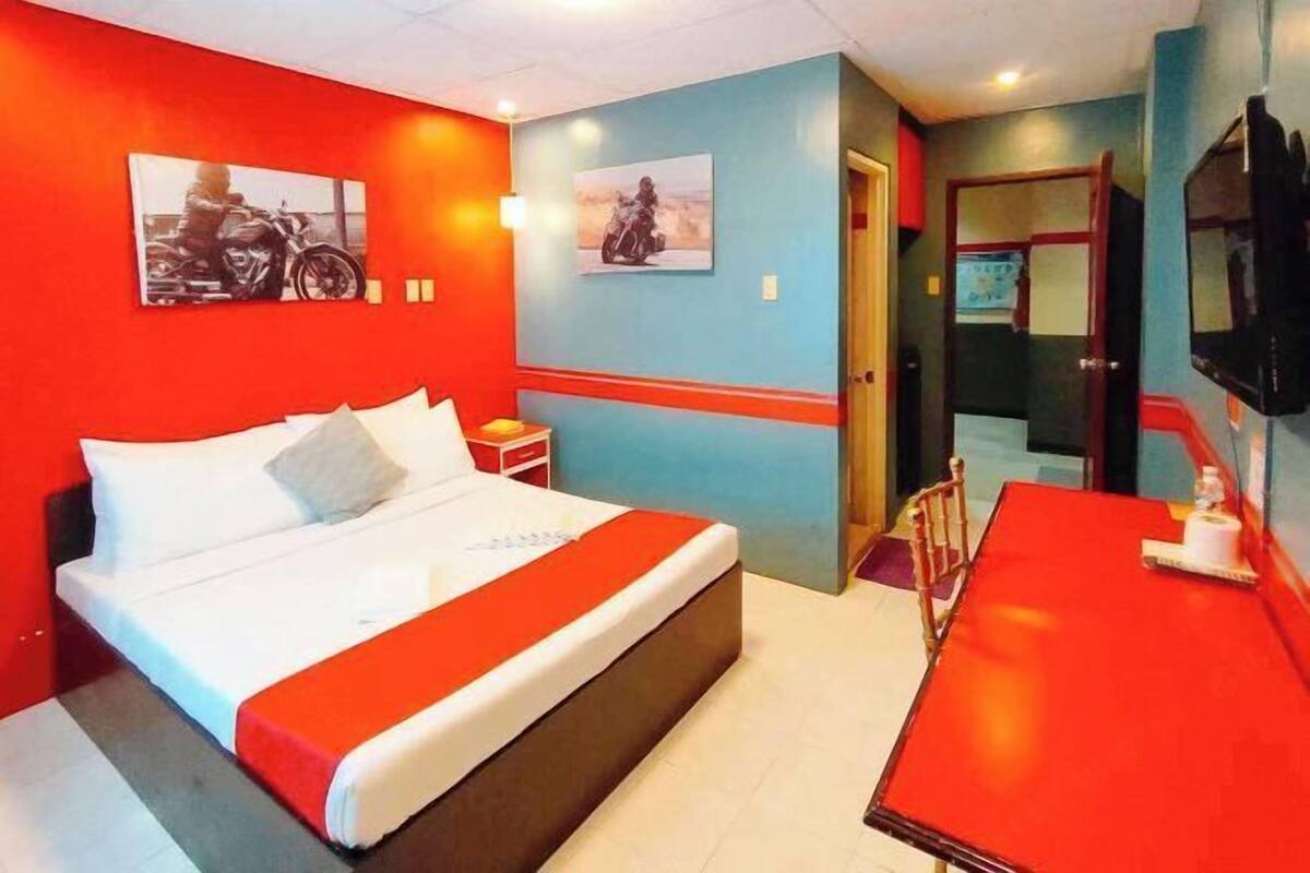 A hotel room with a bed, a desk, and two wall-mounted televisions.