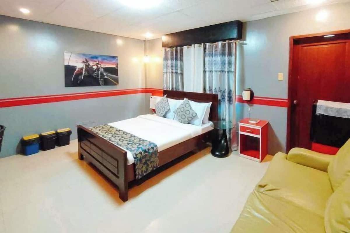 A bedroom with a bed, bedside table, curtains, a painting, and a red-striped wall.