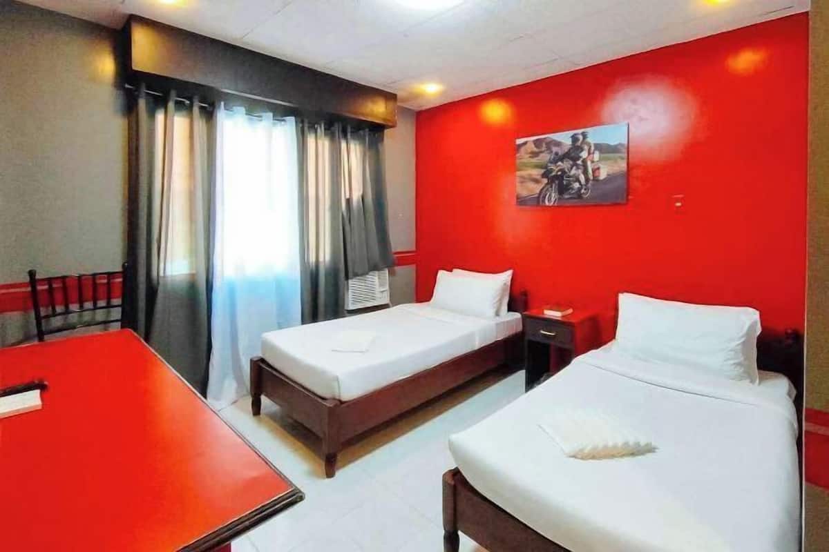 A hotel room with two beds, a red table, and a painting on the wall.