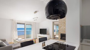 A modern kitchen with a black stove, a dining area with a white table, and a TV on a white cabinet. - Villa Sandra - Private Pool (Pisak)