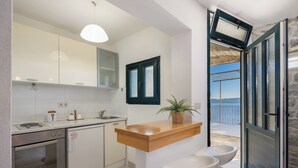 A modern kitchen with white cabinets, a wooden countertop, and a view of the sea through an open door. - Villa Sandra - Private Pool (Pisak)