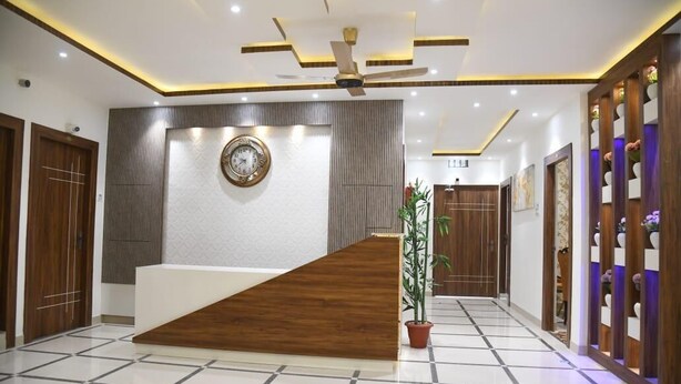 A reception area with a wooden reception desk, a clock on the wall, and a potted plant. - Cozy hotel in terrific Purnia with WiFi, AC (Purnia)