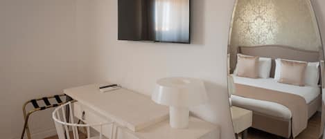 A modern hotel room with a bed, a desk with a chair, a television, and a large mirror.