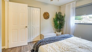 A bedroom with a bed, a ceiling fan, a door, a potted plant, and a window. - Dtwn Palm Harbor Condo: Walk to Water! (Palm Harbor)