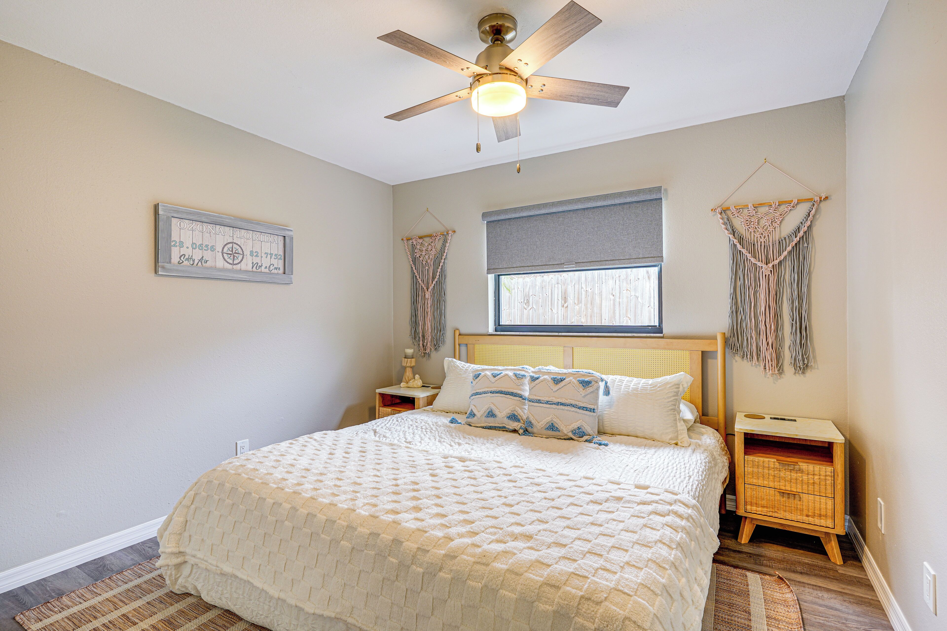 A bedroom with a bed, a ceiling fan, a window with blinds, and a nightstand with a lamp.