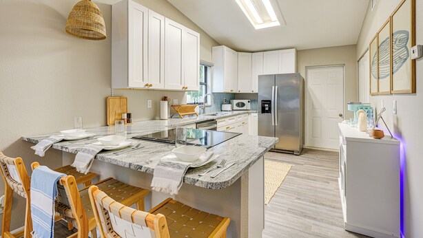 A modern kitchen with white cabinets, a marble countertop, and a central island. - Dtwn Palm Harbor Condo: Walk to Water! (Palm Harbor)