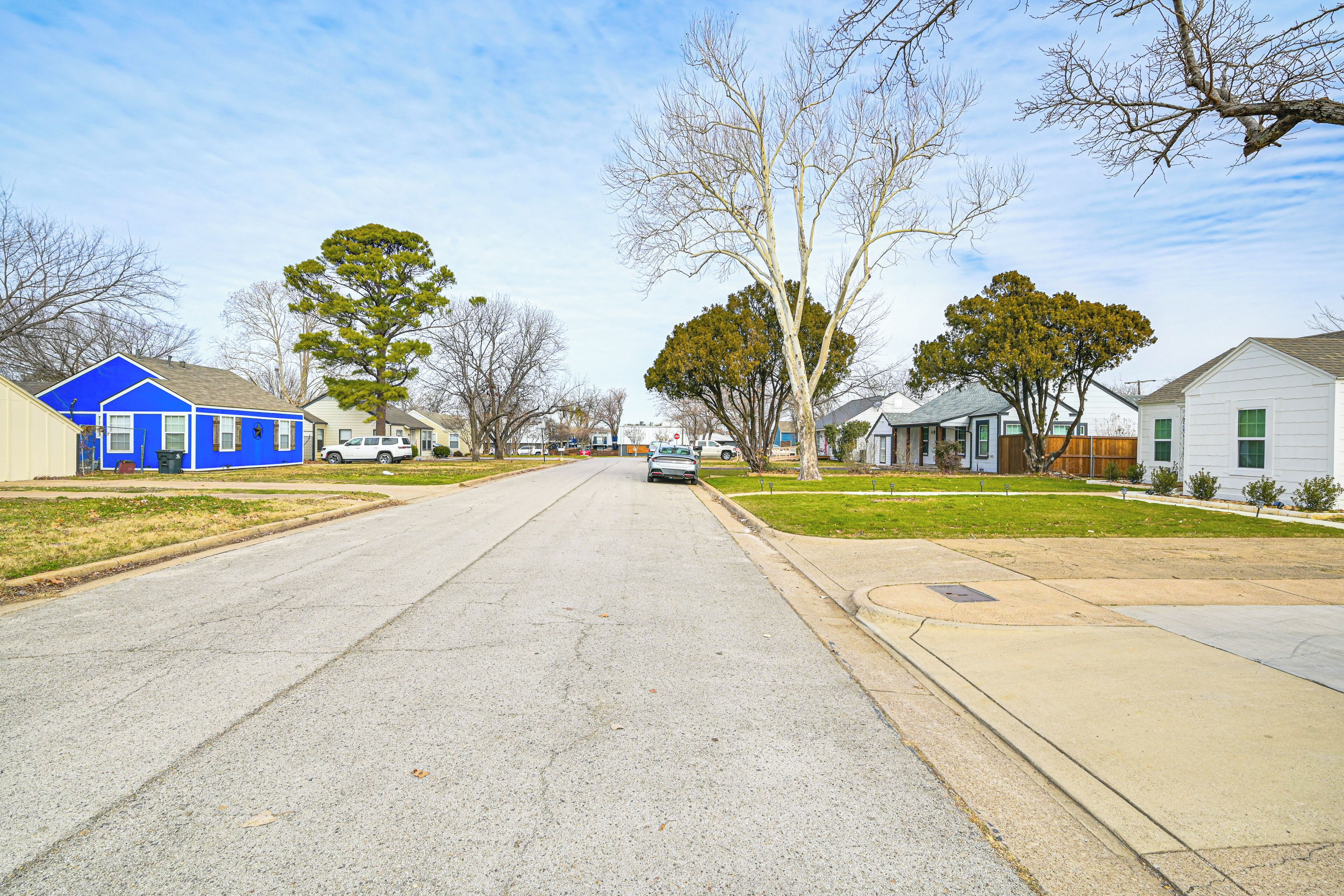 A residential street with houses, a sidewalk, and a car parked on the side.