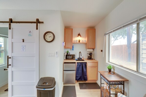 A compact kitchen with a microwave, sink, and double oven. There is a clock on the wall and a window providing natural light.
