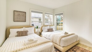 A bedroom with two beds, a large window, and a framed artwork on the wall.