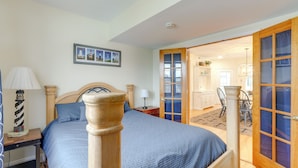 A bedroom with a bed, a nightstand, a lamp, and a door leading to a dining area. - < 1/2 Mi to Boardwalk: Roomy Wildwood Retreat! (North Wildwood)