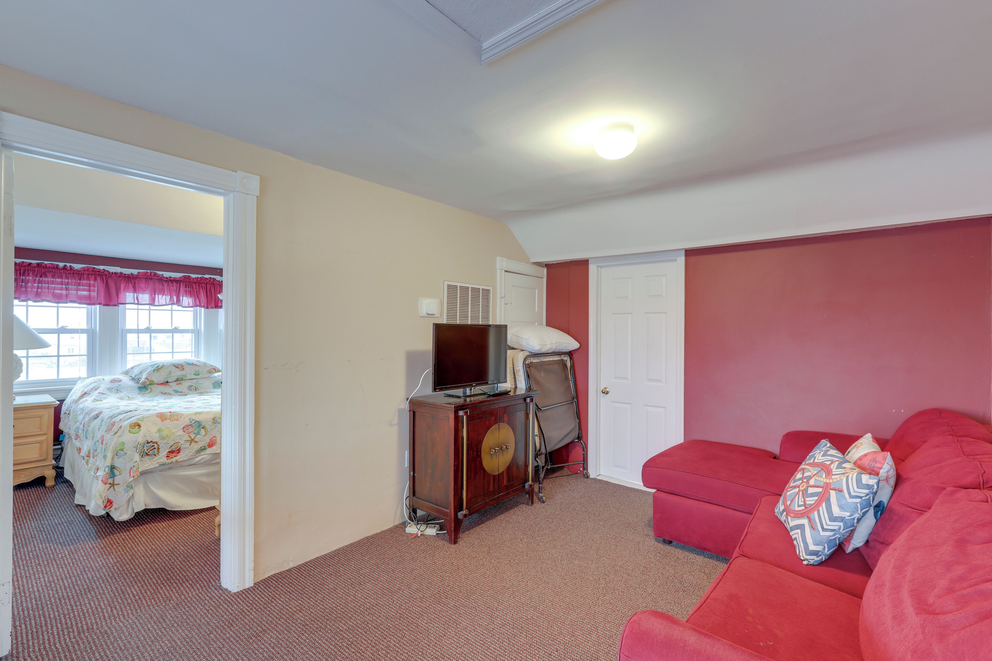Quarto com cama, penteoudeiro com televisão, sofá vermelho e uma porta.