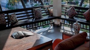 A modern interior with a high ceiling, a chandelier, a bench with patterned cushions, and a view of the outside. - Maison De Chiangrai (Chiang Rai)