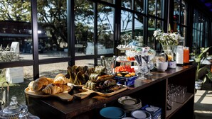 A buffet table with various food items and glassware, set against a backdrop of large windows overlooking a garden. - Maison De Chiangrai (Chiang Rai)