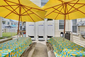 Un área junto a la piscina con sombrillas amarillas, sillas de madera para tomar el sol y una mesa de billar.