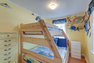 Una cama litera con estructura de madera, un aparador pequeño con cajones, y una pared decorada con motivos náuticos.
