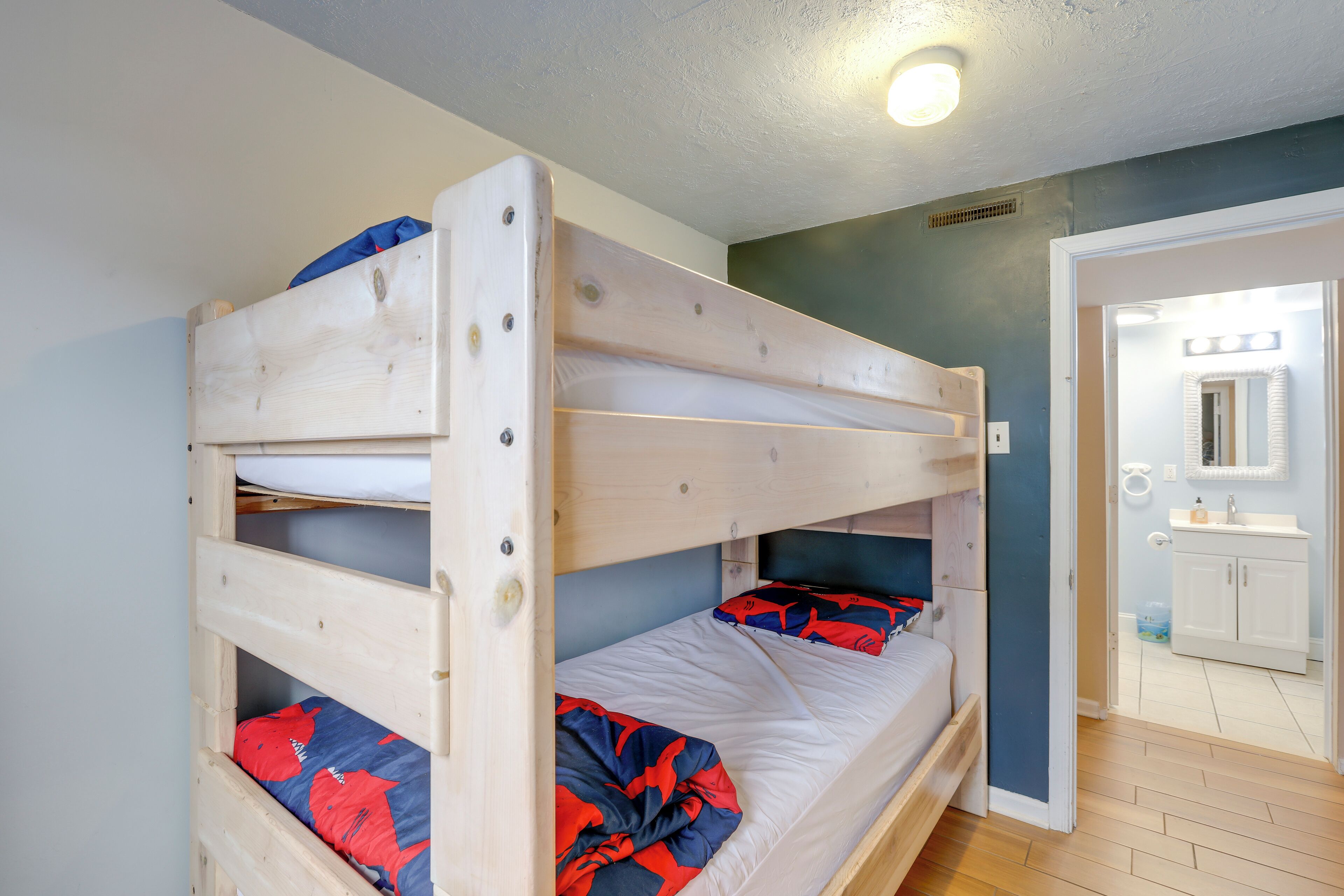 Un lit superposé avec une literie rouge et bleue, une tête de lit en bois et un mur de couleur claire.